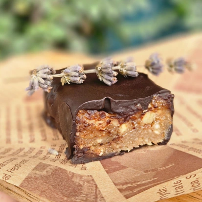 An artisanal vegan dessert bar made with cashews, figs, raisins, dates, walnuts, and dark chocolate, displayed on a rustic wooden surface.